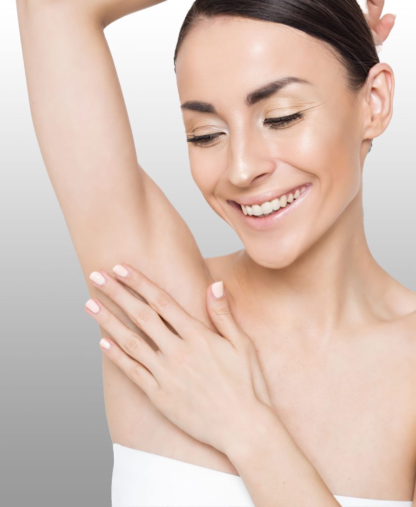 A smiling woman raising her arm and feeling her smooth armpit.