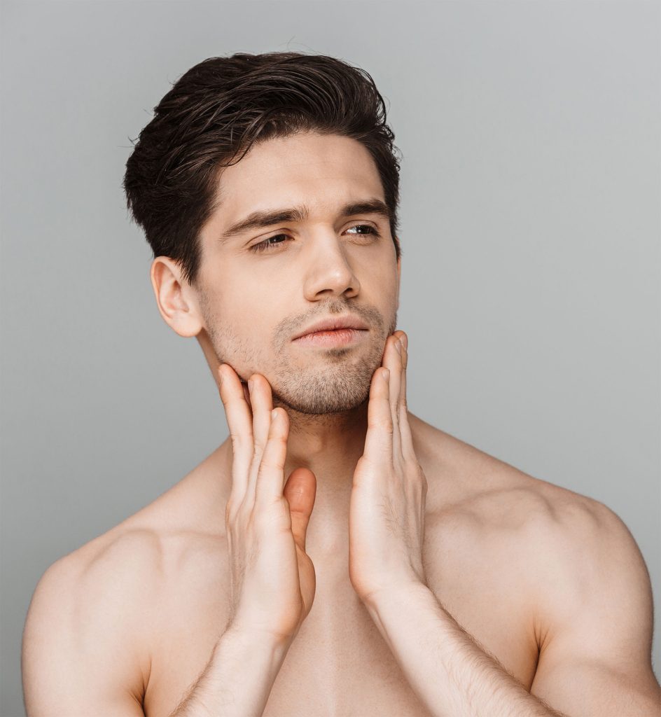 A male model gazes thoughtfully into the distance, his hands gently brushing against his face.